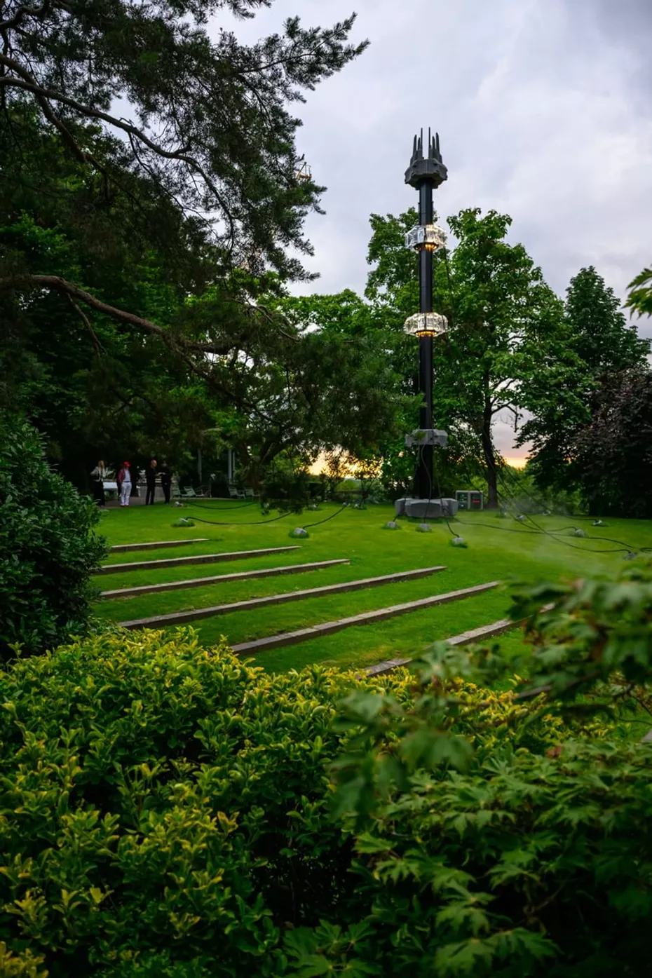 Vue d’une installation sculpturale dans un parc verdoyant à LUMA Arles, avec une structure noire et lumineuse au centre.