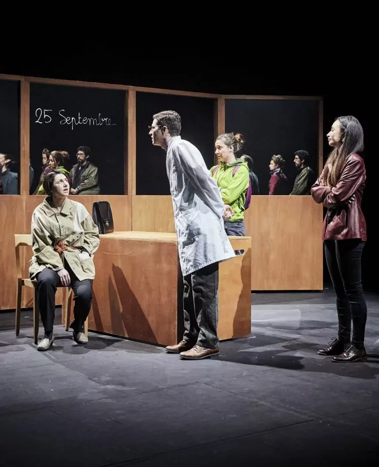 Scène de théâtre au Théâtre Paris-Villette : un groupe d'acteurs incarne élèves et enseignants dans une salle de classe.